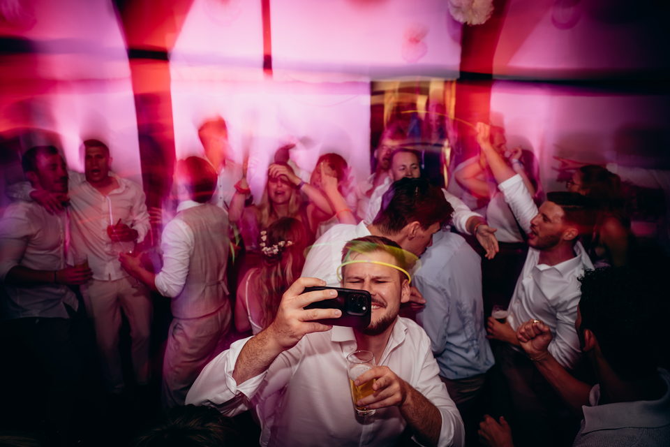 Ein Gast hält die Kamera hoch, ringsum tanzende Menschen im pinken Licht